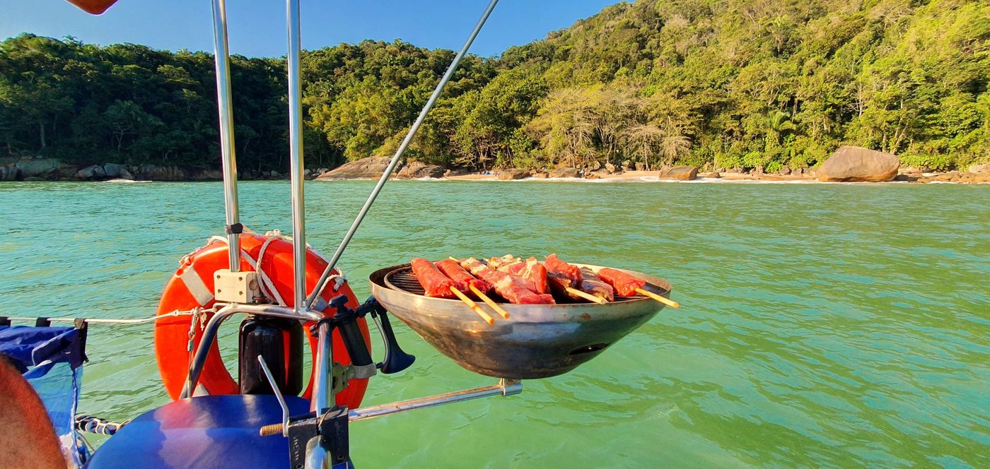 Churrasqueira a bordo com espetinhos, diante de uma praia de águas verdes