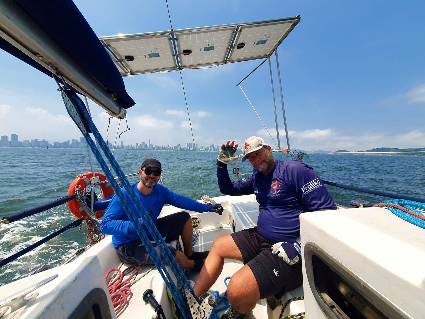 Tripulantes no cockpit do Éolo durante uma regata, com a cidade de Santos ao fundo