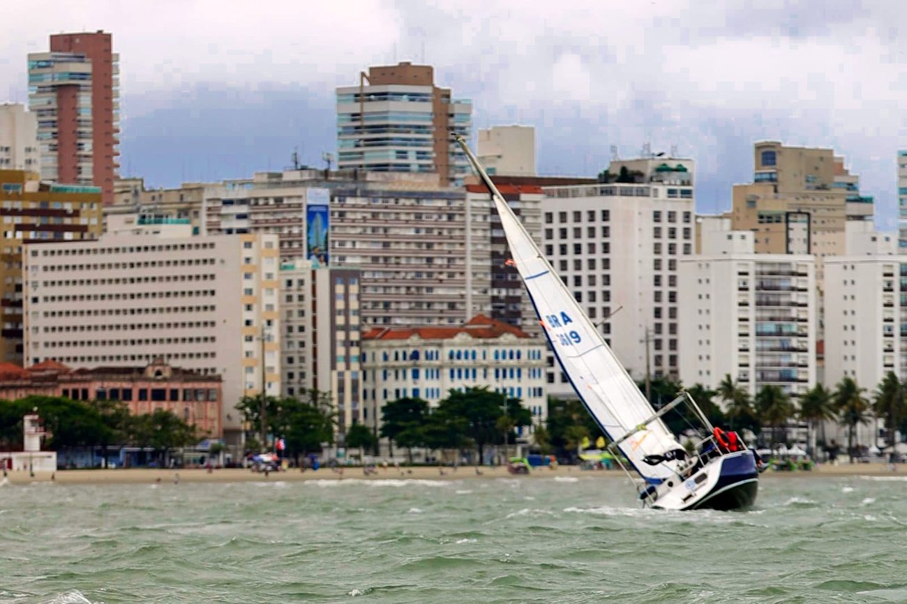 O Éolo inclinado pelo vento diante dos prédios da orla de Santos